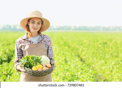 Female farmer holding wicker bowl with vegetables in field