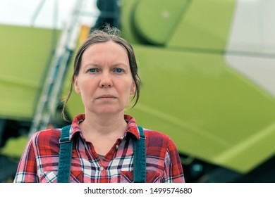 Female Farmer Posing In Front Of Combine Harvester. Serious Woman Farm Worker With Agricultural Machinery Ready Harvest Crops.