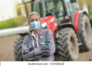 Female farmer standing in front of a tractor and wearing a protective mask against covid-19
