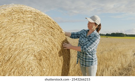 Female Farmer Touches And Checks Bales Of Hay In Countryside At Sunset. Woman Standing Near Hay Bale In Summer Evening In Field. Gimbal shot. - Powered by Shutterstock