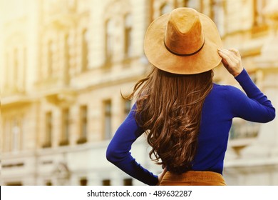  Female fashion concept. Outdoor portrait of young beautiful fashionable lady walking on the street. Model wearing stylish hat and clothes. Sunny day. Back view. Waist up. Copy space for text