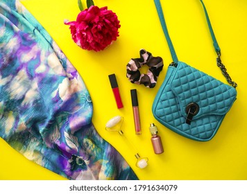 Female fashion and cosmetic accessories. Green woman bag, lipsticks, serum, facial roller, nail polish, silk scarf and on illuminating yellow background with peony flower. Overhead view girl concept
