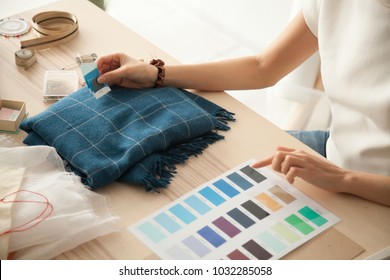 Female fashion designer holding color samples choosing fabric textile blue shades at workplace, dressmaker or tailor working at desk pointing at set palette making choice selection, close up view