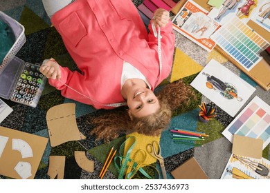 Female fashion designer with supplies lying on carpet in studio, top view - Powered by Shutterstock