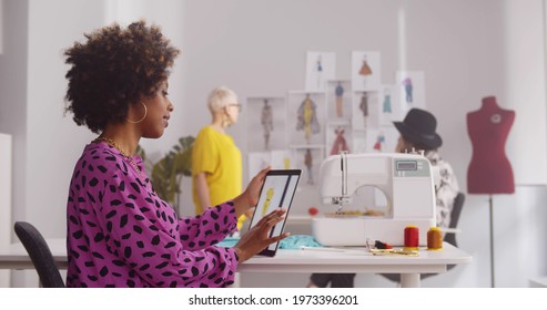 Female fashion designer using digital tablet in creative office. Portrait of young afro-american female tailor studying sketches on tablet pc siting at desk in modern atelier - Powered by Shutterstock