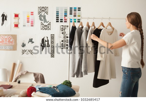 Female fashion designer works on new womenswear\
collection for clients in cozy workshop studio, dressmaker, tailor\
or needlewoman standing near clothing rack with fashionable stylish\
handmade clothes