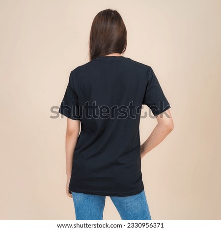 Female fashion model in black t-shirt and jeans standing in studio on beige background, trendy clothing style, copy space