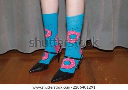 female feet in bizarre giraffe blue socks with pink donuts and classical black shoes, eclectic style