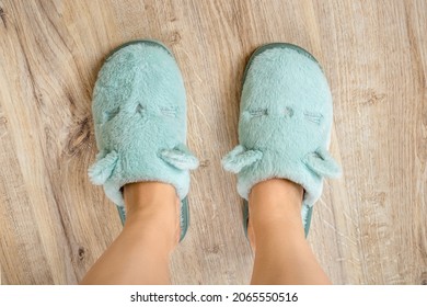 Female Feet In Blue Cozy Slippers On A Wooden Floor At Bedroom Close-up. Concepts Of Comfy Soft Fleece Home Shoes And Warm Domestic Footwear. Top View.