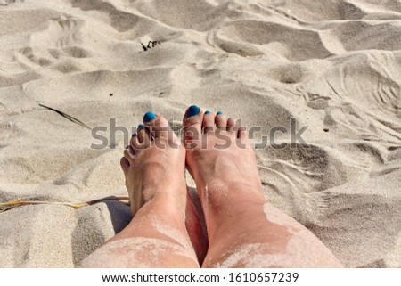 Female feet with blue nails on the sandy beach