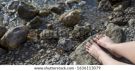 Female feet with colored pedicure on summer sea background. Rocky coast of the black sea. Panoramic banner. 