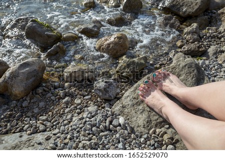 Female feet with colored pedicure on summer sea background. Rocky coast of the black sea.