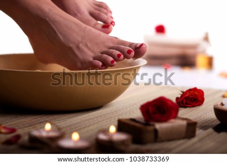 Female feet with drops of water, spa bowl, towels, flowers, candles, sea salt and bottle with essential oil on white background. Foot spa concept.