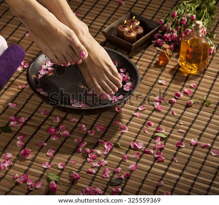 Female feet with drops of water, spa bowl, towels, flowers and candles.