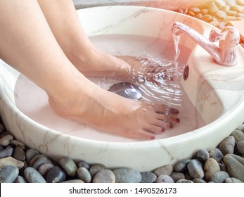 Female feet in foot spa marble basin with water flowing from faucet. Epsom salt foot soak concept.