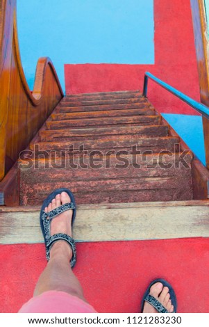 Female feet in front of the stairs down. Below the floor is red-blue
