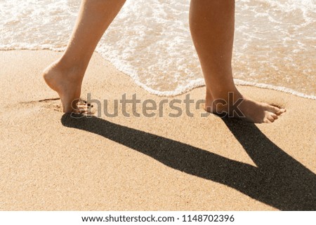 Female feet go along the line of the sea surf on wet sand, close-up