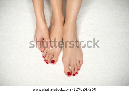 Female feet and hand on white terry towel. Woman holds her sole and mass it by her fingers. Classic French manicure and red pedicure. SPA and skin care concept.