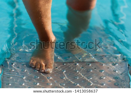 Female feet on the steps of the pool