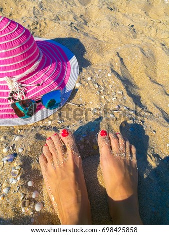 Female feet with red nails, pink hat and blue sunglasses on a sandy beach