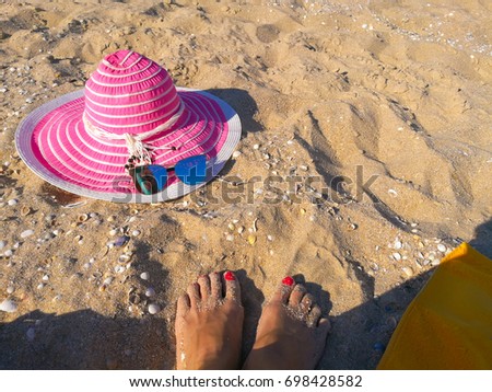 Female feet with red nails, pink hat and blue sunglasses on a sandy beach