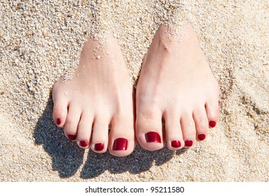 female feet with red pedicure in beach sand