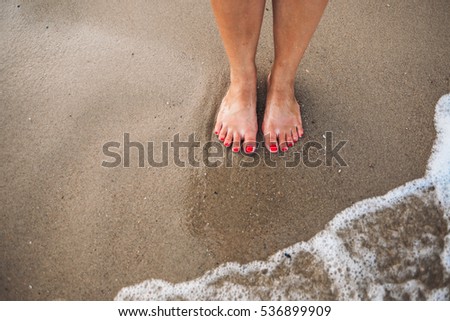 Female feet with red polish on nails on the beach