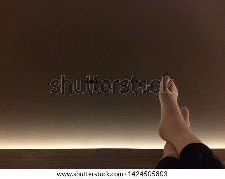 Female feet rest on top of board in front of dark brown wall. Space for text