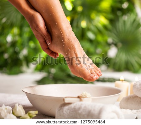 Female feet with sea salt on white floor and tropical green leaves background