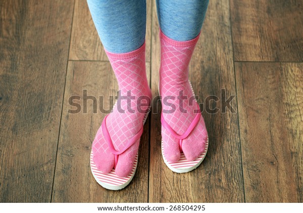 Female feet in socks with pink flip-flops, on\
floor background
