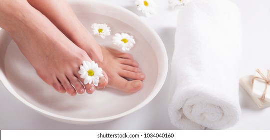 Female feet with spa bowl, towel and flowers on white background