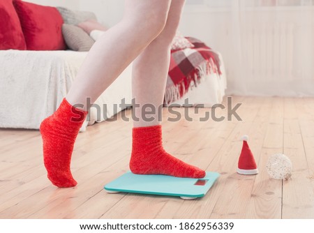 Female feet standing on blue electronic scales for weight control in red socks with Christmas decoration