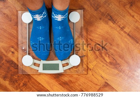 Female feet standing on electronic scales for weight control in Christmas socks on wooden floor background. with copy space. top view