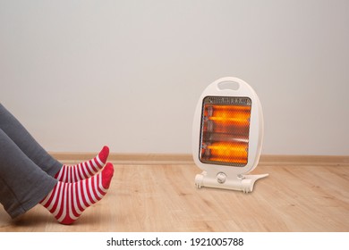 female feet standing on parquet floor, in front of halogen heater - Shutterstock ID 1921005788