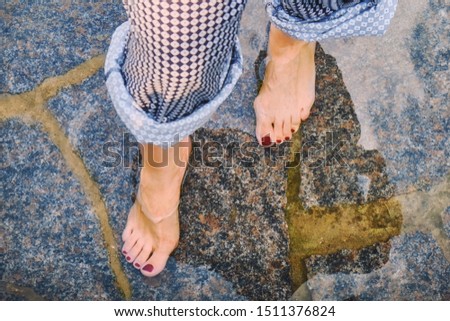 Female feet in the water on the flooded shore, close-up. The girl stands on a rocky shore after the surf.