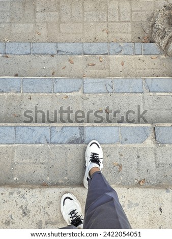 Female feet wearing grey trousers and white sneakers, stepping on the paving block stairs with crisscrossing pattern.