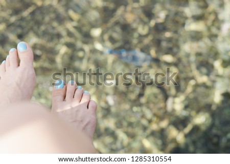 Female feets with a blue pedicure on a blurred background of the sea with a floating fish. Vacation at sea