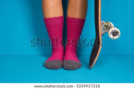 Female feets with pink socks and a skateboard. Blue background.
