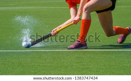 Female field hockey player passing to a team mate on a modern, water artificial astroturf field