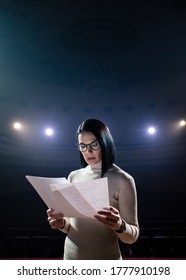 The Female Financial Coach Emotional Gesturing Talks From The Stage With Spectators At Forum. Too Many Anonymous Persons Workers And Students Seat In Large Auditorium And Watch Workshop Background