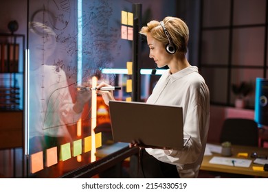 Female Financial Expert, Ceo Manager Working Near Scrum Kanban Glass Wall And Writing Ideas. Blond Woman In Headset, Using Laptop And Consulting With Colleague On Video Call