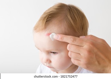 Female Finger Applying Medical Ointment On Baby Abrasion Skin. Mother Giving First Aid. Infant Head Closeup Isolated On Gray Background.