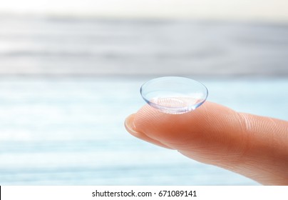 Female finger with contact lens on blurred background