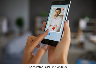 Female Finger Pushing Chat Button On Smartphone Using Dating App To Find Love And Online Connection. Focus On Handsome Man Profile Photo On Screen. Modern Lifestyle Relationship, Remote Relation