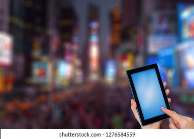 Female Finger Touching Tablet Blue Blank Touchscreen Ready For Your Text. Intentionally Blurred Image Of A Night Times Square (NYC) Is In The Background. All Potential Trademarks Are Removed.