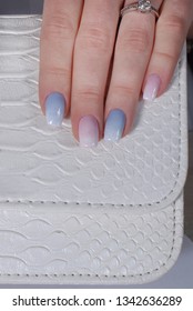 Female fingers and beautiful gradient manicure in pink   blue colors lie the top white handbag  Studio light 