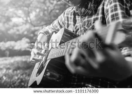 Female fingers playing guitar outdoor in summer park. 