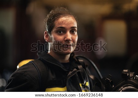 female firefighter portrait wearing full equipment and emergency rescue equipment. taking off oxygen mask after successful intervention. fire trucks in the background. 
