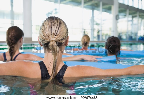 Female fitness class doing\
aqua aerobics with foam rollers in swimming pool at the leisure\
centre