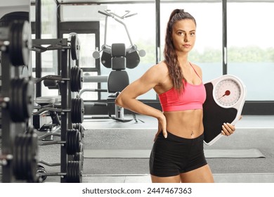 Female fitness coach holding a weight scale at a gym - Powered by Shutterstock